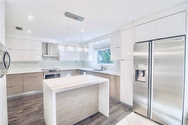 kitchen with pendant lighting, appliances with stainless steel finishes, white cabinetry, tasteful backsplash, and wall chimney exhaust hood