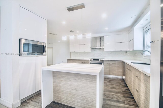 kitchen featuring appliances with stainless steel finishes, pendant lighting, white cabinetry, sink, and wall chimney range hood