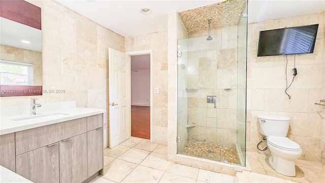 bathroom featuring a shower with door, vanity, tile walls, and toilet