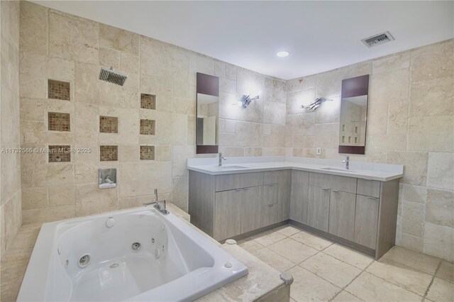 bathroom featuring tiled tub, vanity, and tile walls