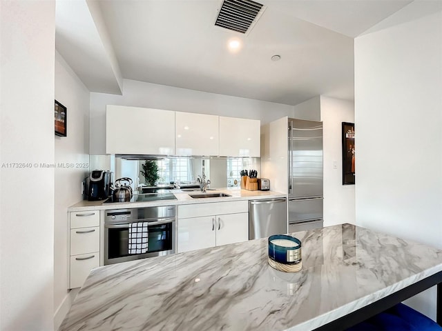 kitchen with appliances with stainless steel finishes, a breakfast bar, white cabinetry, sink, and kitchen peninsula