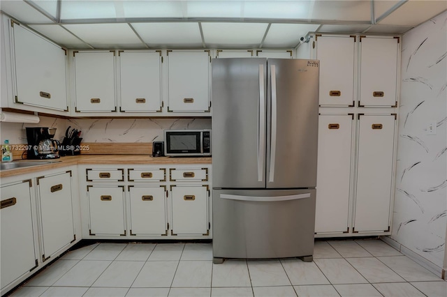 kitchen with stainless steel refrigerator, sink, light tile patterned floors, and white cabinets