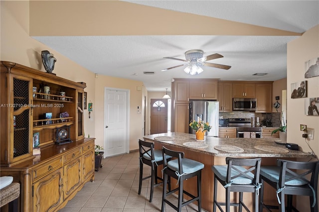 kitchen featuring a breakfast bar area, tasteful backsplash, light tile patterned floors, appliances with stainless steel finishes, and kitchen peninsula