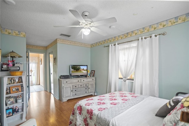 bedroom with a textured ceiling, light hardwood / wood-style flooring, and ceiling fan