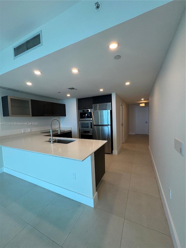 kitchen featuring sink, light tile patterned floors, stainless steel refrigerator, double oven, and kitchen peninsula