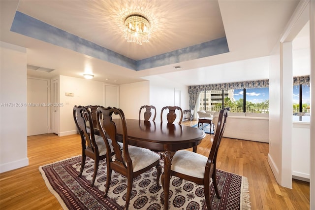 dining area featuring an inviting chandelier, a tray ceiling, and light hardwood / wood-style floors