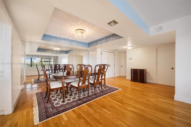 dining area featuring a raised ceiling, a chandelier, and light wood-type flooring