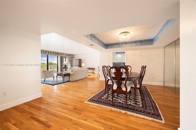 dining room with a notable chandelier, hardwood / wood-style flooring, and a raised ceiling