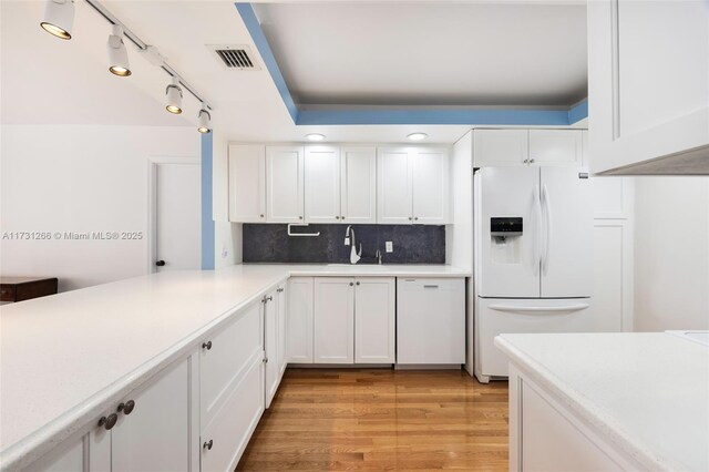 kitchen with tasteful backsplash, white cabinetry, sink, white fridge with ice dispenser, and light wood-type flooring