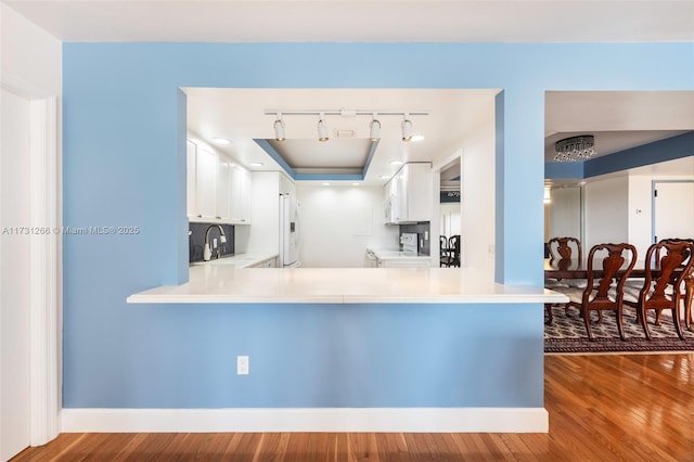 kitchen with dark wood-type flooring, sink, white cabinets, and kitchen peninsula