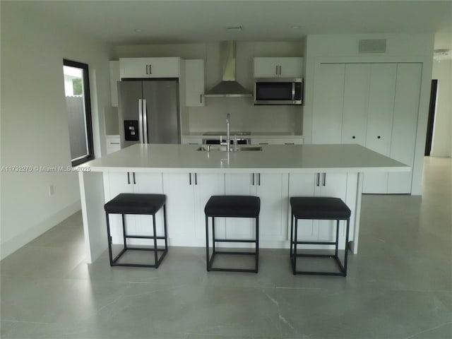 kitchen featuring wall chimney exhaust hood, white cabinetry, a kitchen breakfast bar, stainless steel appliances, and a large island