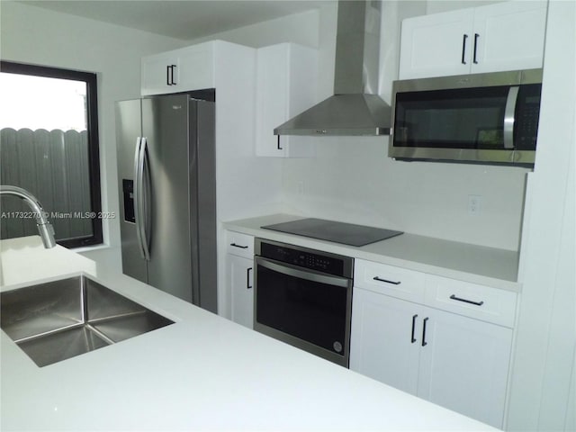 kitchen with white cabinetry, stainless steel appliances, sink, and wall chimney range hood