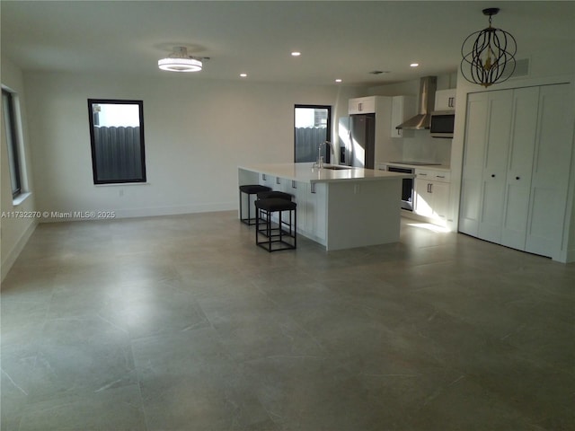 kitchen with pendant lighting, stainless steel appliances, white cabinets, a center island with sink, and wall chimney exhaust hood