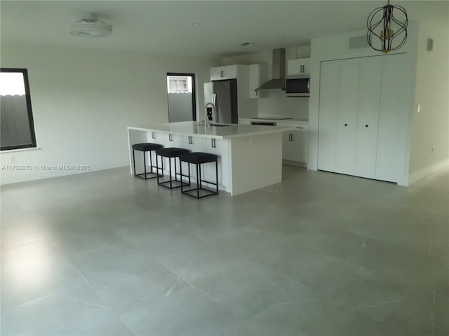 kitchen with wall chimney exhaust hood, decorative light fixtures, appliances with stainless steel finishes, an island with sink, and white cabinets