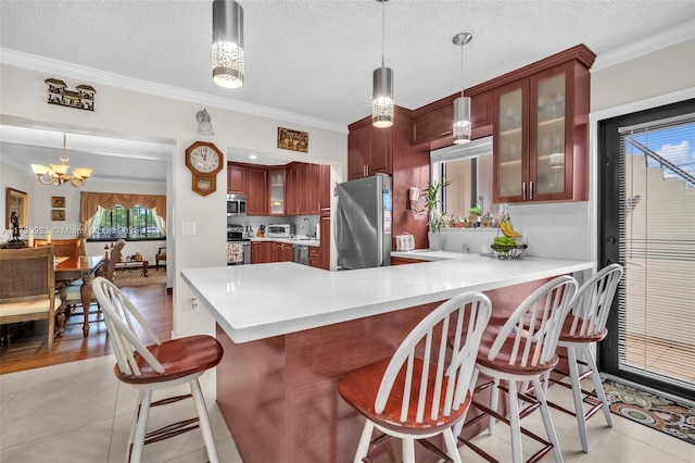 kitchen featuring appliances with stainless steel finishes, decorative light fixtures, a kitchen bar, kitchen peninsula, and crown molding