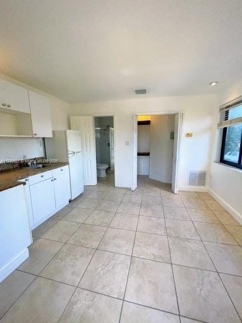 kitchen featuring white refrigerator, light tile patterned floors, and white cabinets