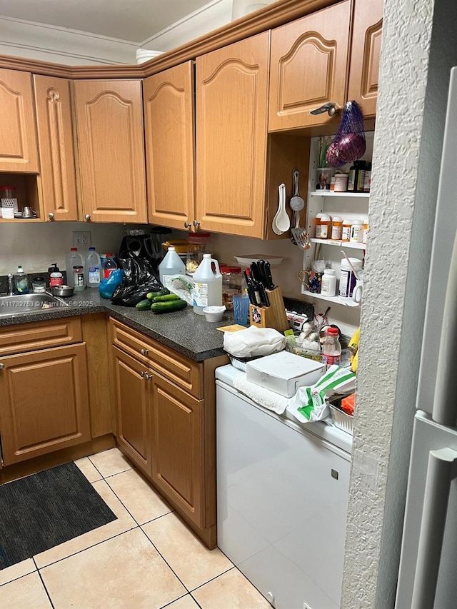 kitchen featuring ornamental molding, sink, light tile patterned floors, and refrigerator