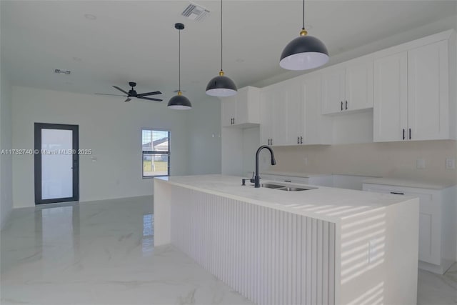 kitchen with an island with sink, sink, pendant lighting, and white cabinets