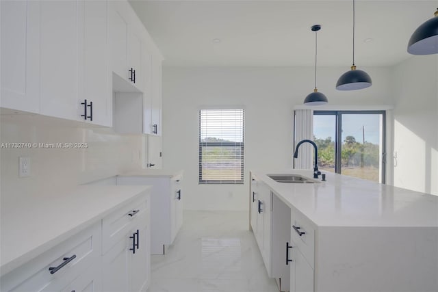 kitchen featuring sink, white cabinetry, an island with sink, pendant lighting, and decorative backsplash