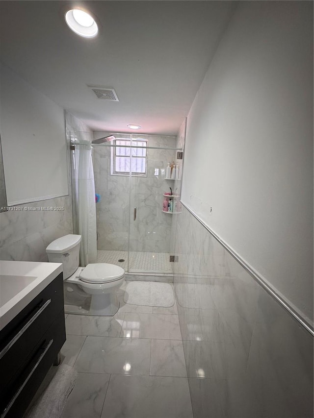 bathroom with vanity, a shower with door, toilet, and tile walls