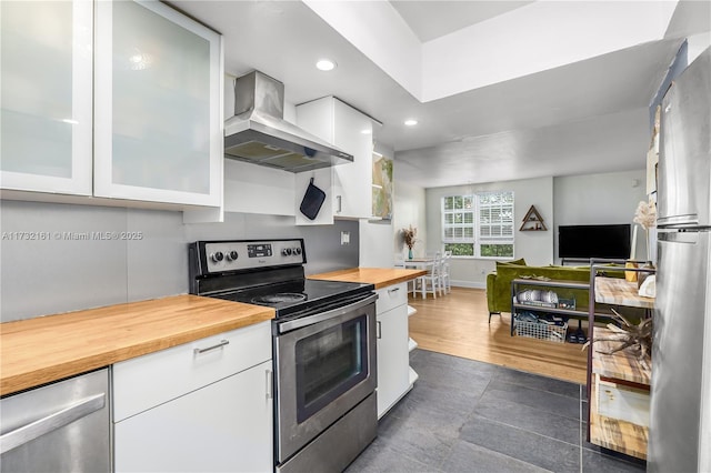 kitchen with butcher block counters, white cabinets, wall chimney exhaust hood, and appliances with stainless steel finishes