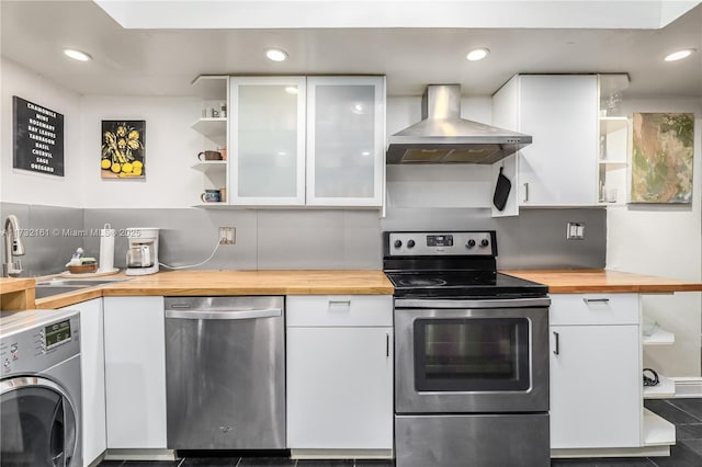 kitchen featuring wood counters, wall chimney exhaust hood, appliances with stainless steel finishes, washer / clothes dryer, and white cabinets