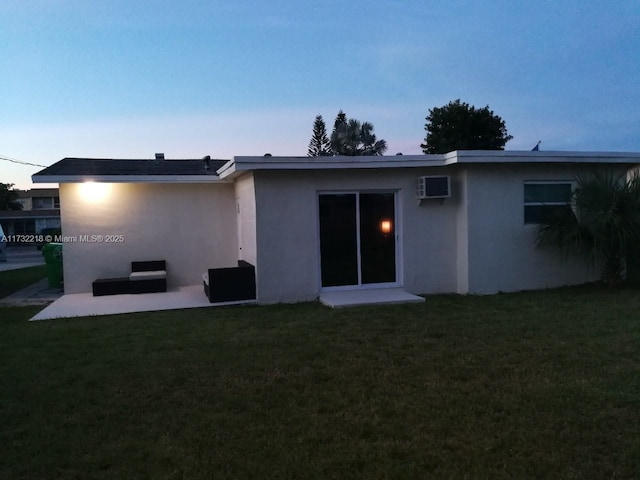 back house at dusk featuring a yard and a wall mounted AC