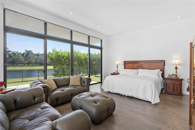 bedroom with a water view, access to outside, hardwood / wood-style floors, and a wall of windows