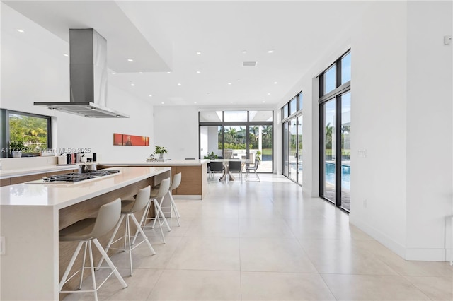 kitchen with light tile patterned flooring, floor to ceiling windows, a breakfast bar, stainless steel gas cooktop, and island exhaust hood