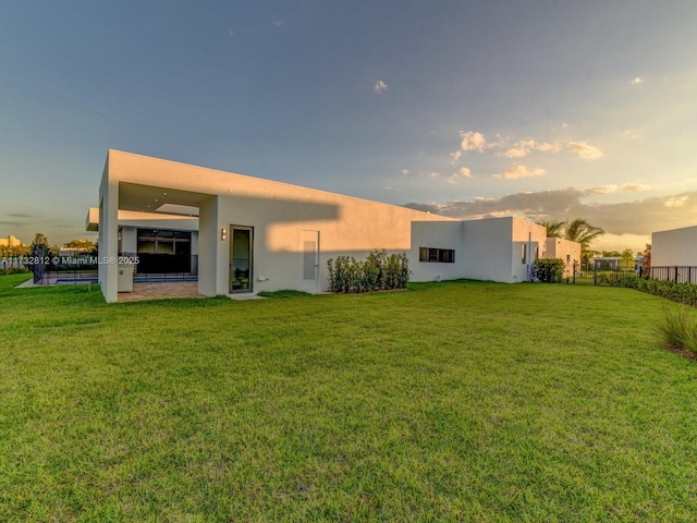 back house at dusk featuring a lawn