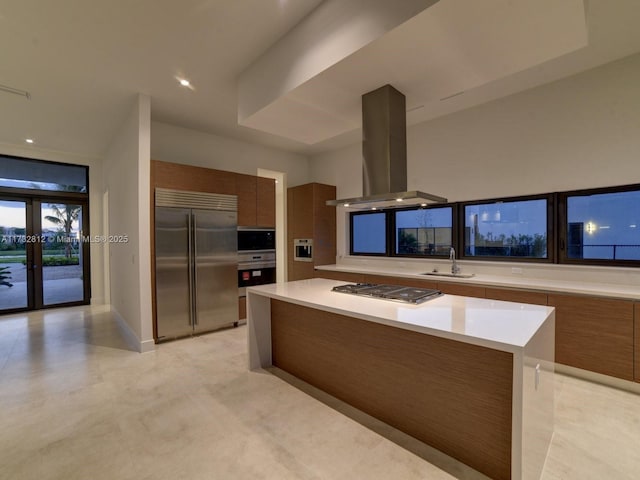 kitchen with sink, island exhaust hood, built in appliances, a kitchen island, and french doors