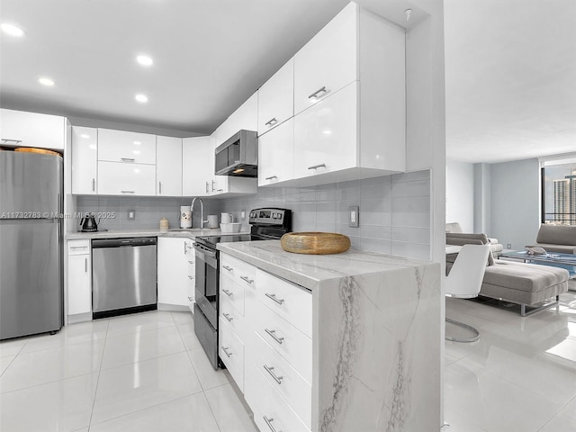 kitchen with light tile patterned flooring, appliances with stainless steel finishes, white cabinetry, sink, and light stone countertops