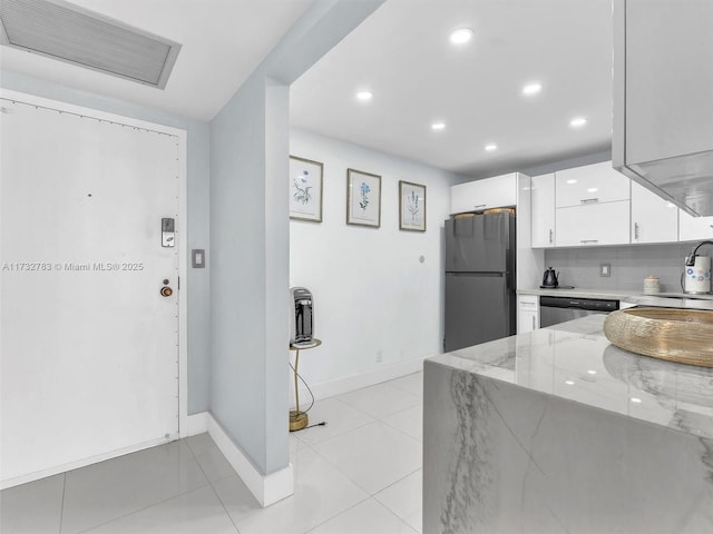 kitchen featuring black refrigerator, white cabinetry, backsplash, light stone counters, and stainless steel dishwasher