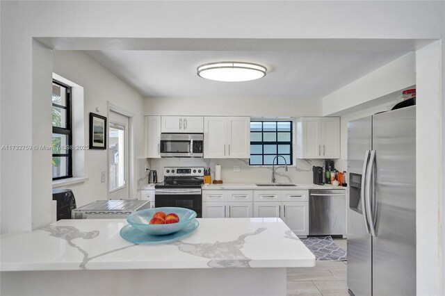 kitchen featuring appliances with stainless steel finishes, white cabinetry, sink, kitchen peninsula, and light stone countertops