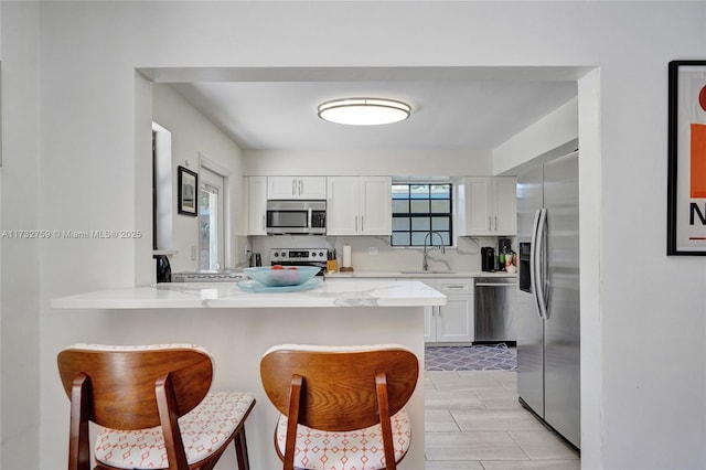 kitchen featuring sink, a breakfast bar, white cabinetry, stainless steel appliances, and kitchen peninsula