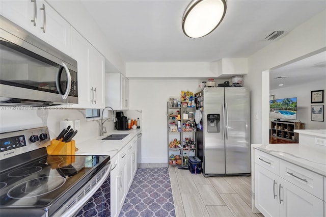 kitchen featuring light stone counters, stainless steel appliances, sink, and white cabinets