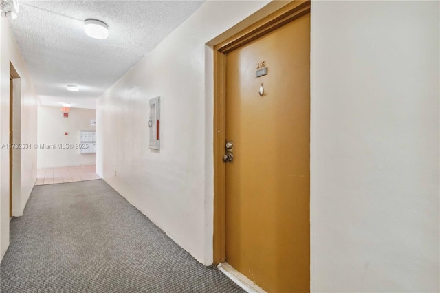 hall featuring a textured ceiling and dark colored carpet