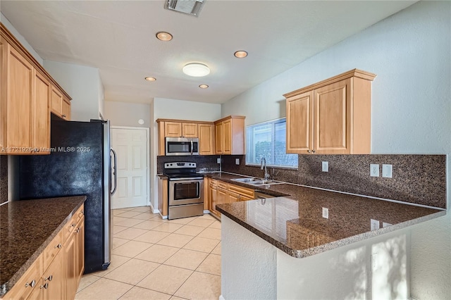 kitchen featuring sink, light tile patterned floors, appliances with stainless steel finishes, kitchen peninsula, and dark stone counters