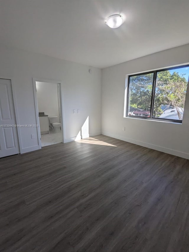 unfurnished bedroom with multiple windows, dark wood-type flooring, and ensuite bathroom