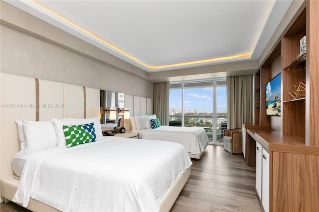 bedroom featuring wood-type flooring, access to exterior, and a tray ceiling