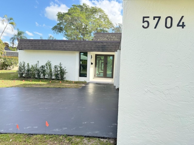 property entrance featuring a shingled roof, mansard roof, and stucco siding