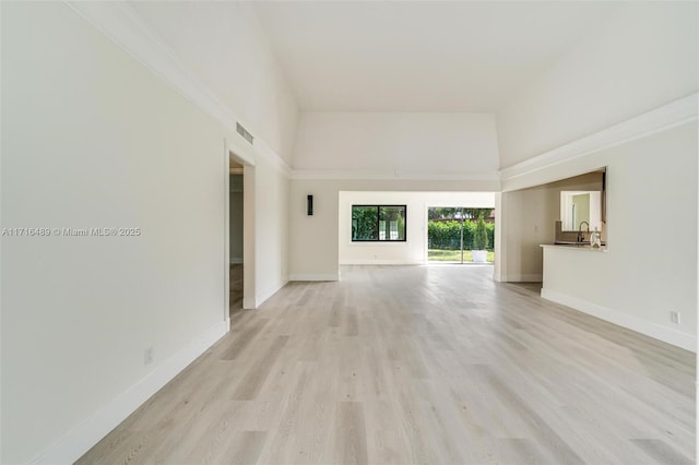 spare room featuring light wood finished floors, visible vents, a towering ceiling, a sink, and baseboards