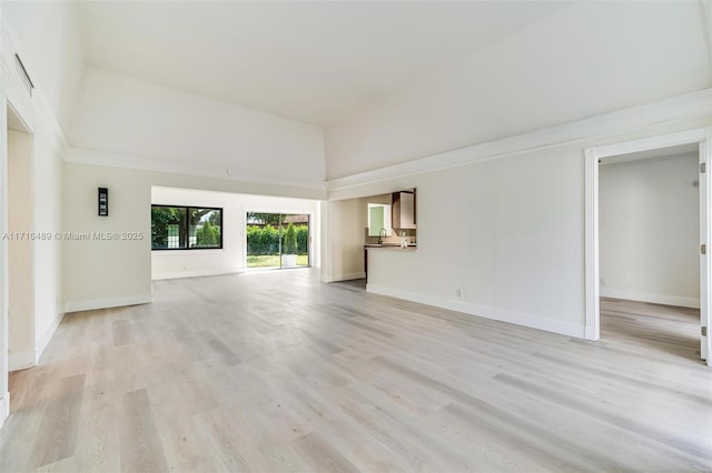 unfurnished living room featuring baseboards, a towering ceiling, and light wood finished floors