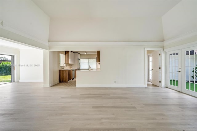 unfurnished living room featuring light wood-style flooring, a sink, a towering ceiling, baseboards, and french doors