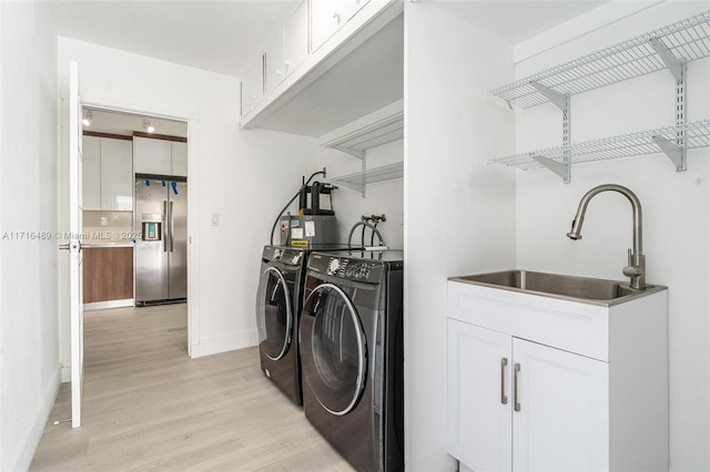 laundry room with light wood finished floors, cabinet space, baseboards, washing machine and clothes dryer, and a sink