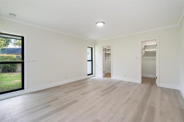 unfurnished bedroom featuring light wood-style floors, baseboards, a walk in closet, and crown molding