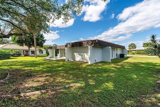 back of property with stucco siding, central AC, a yard, and mansard roof