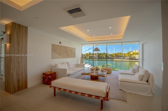 living room with a water view, a wall of windows, a tray ceiling, and light tile patterned floors