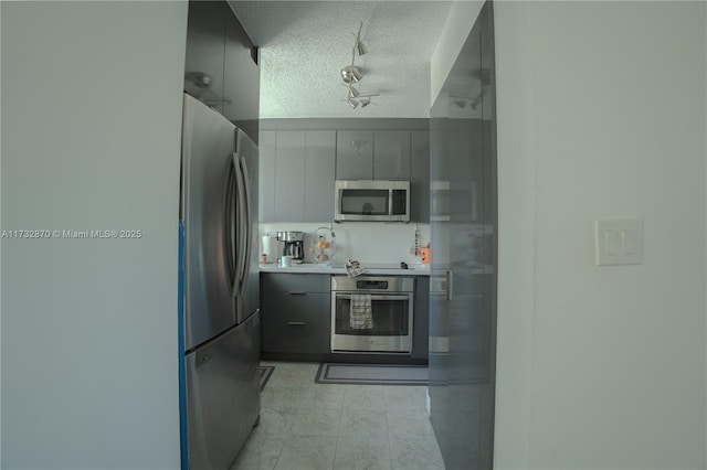 kitchen featuring gray cabinetry, stainless steel appliances, rail lighting, and a textured ceiling