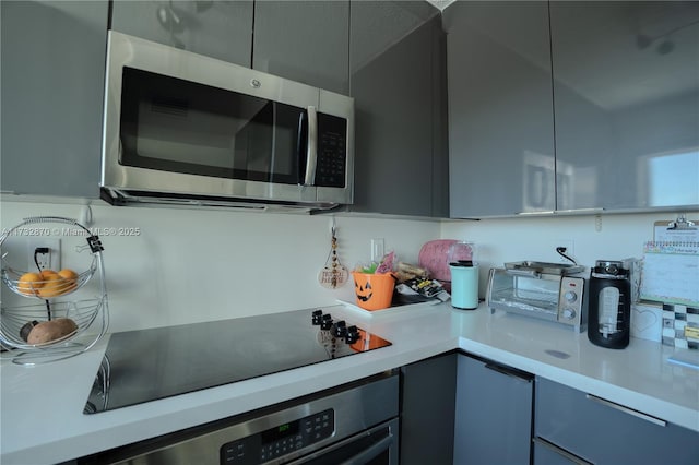 kitchen with backsplash, gray cabinets, and appliances with stainless steel finishes